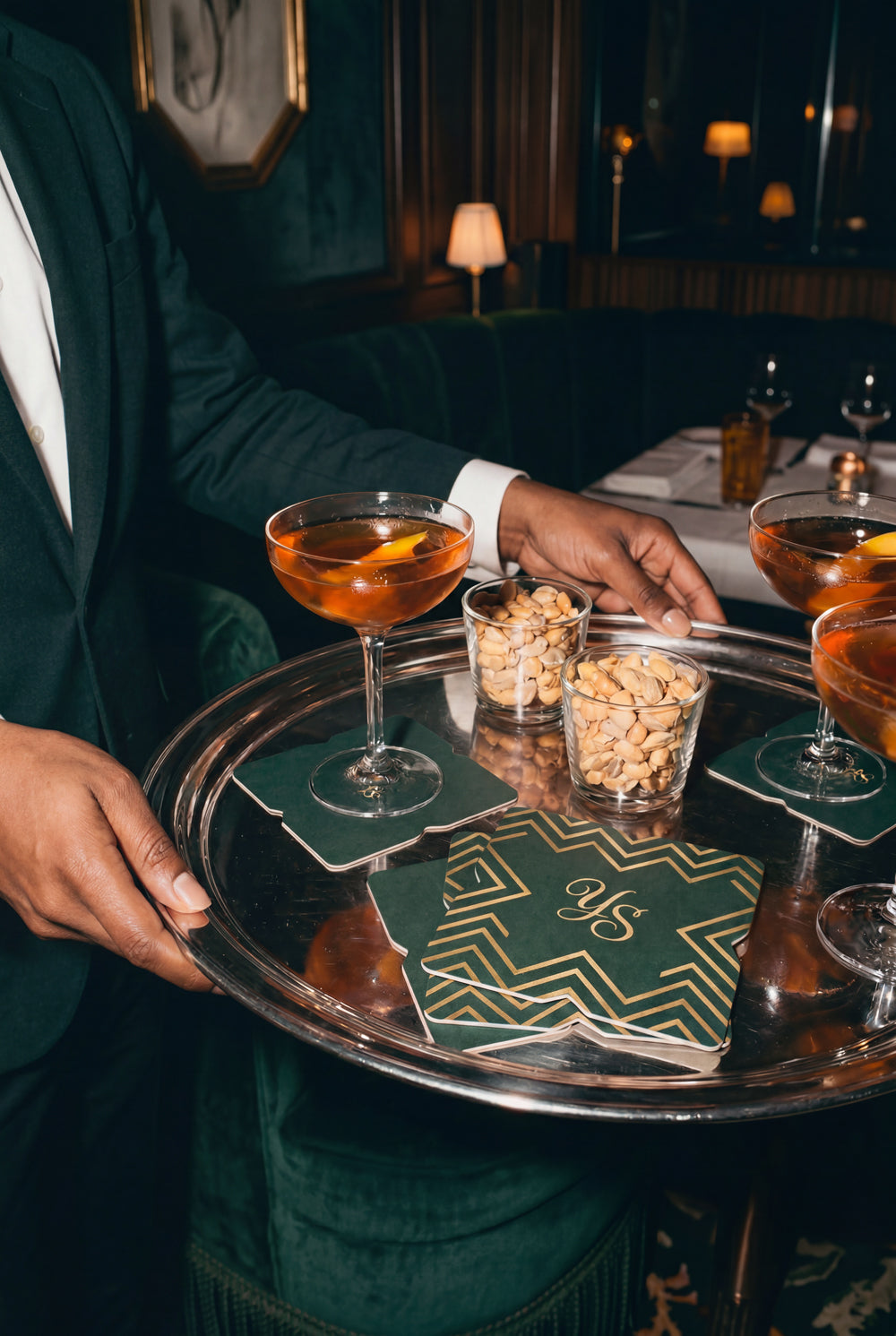 Person holding a tray with cocktails and snacks in a dimly lit bar. Hospitality Branding Agency demonstrates the elegant carry through of interior to branded details.