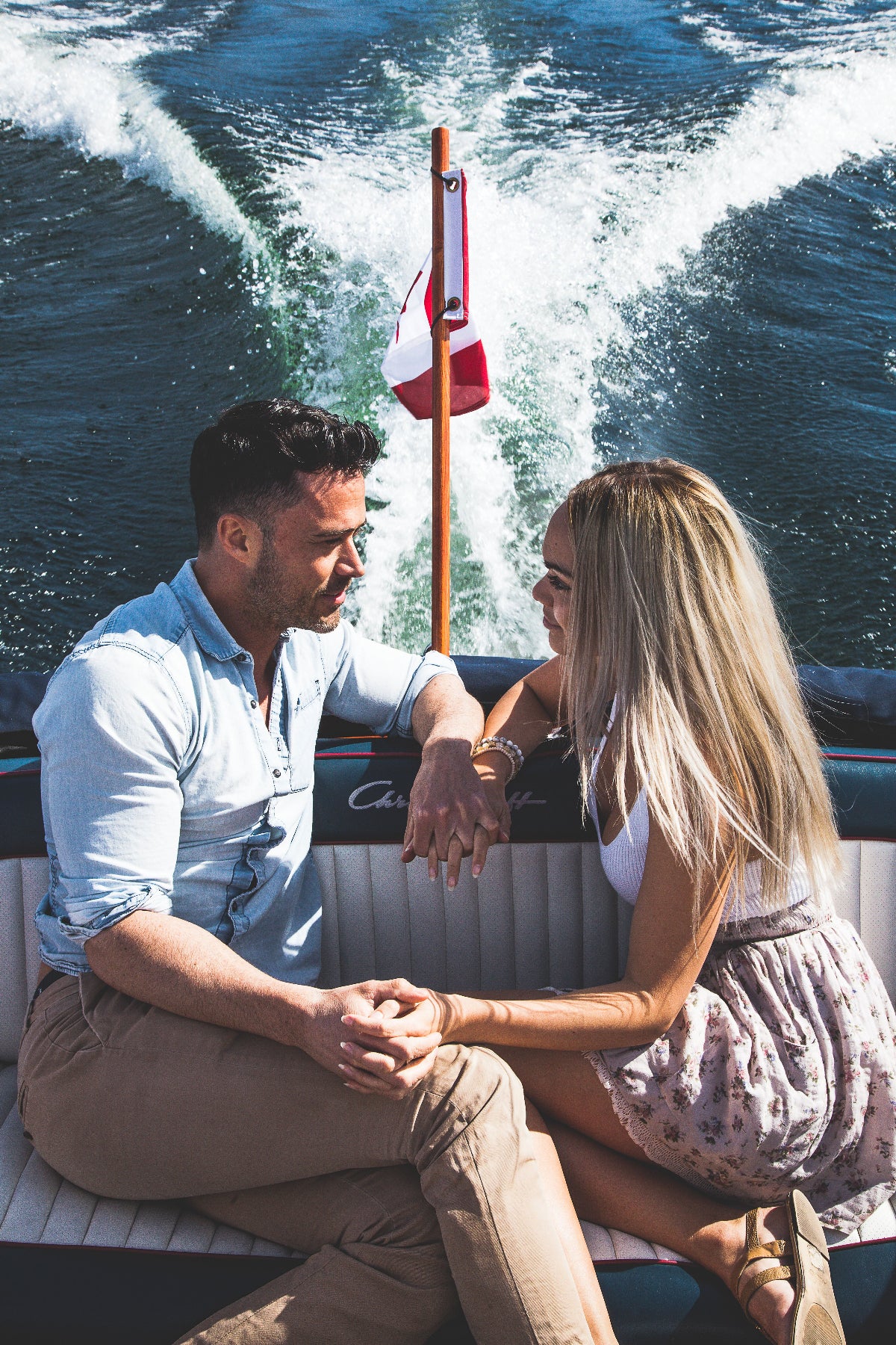 Couple sitting on a vintage boat with a flag in the background, a perfect hospitality experience in the Okanagan for Airbnb Hosts to offer, or for hotels to showcase.