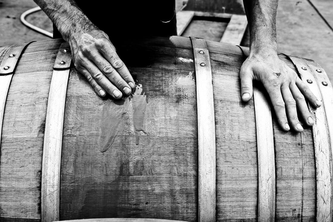 A pair of hands smooths the wooden surface of a large barrel, likely during the process of making or repairing it. The black and white image evokes craftsmanship—an ideal visual for a Winery Branding Agency focused on tradition and detail.