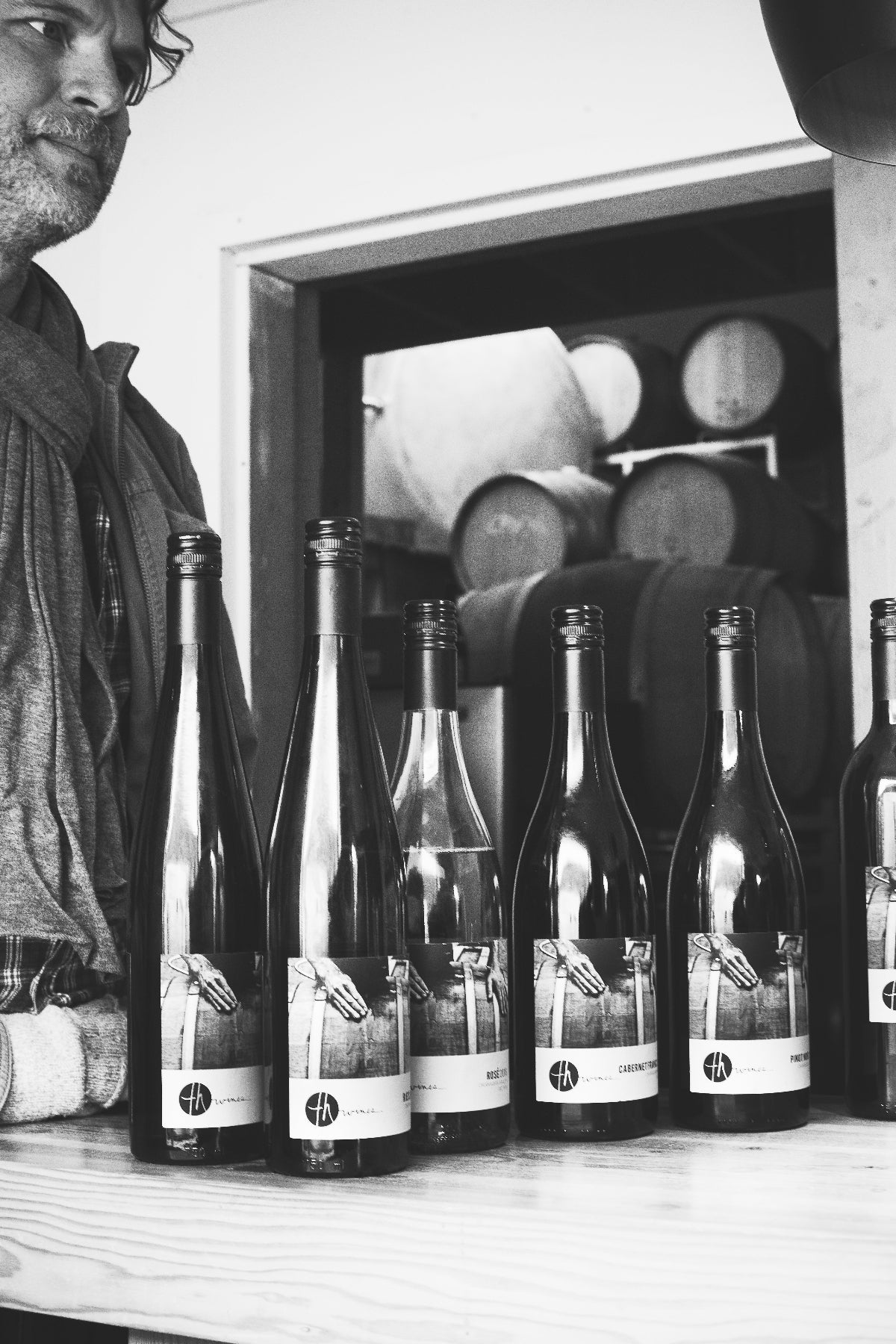 Man standing behind a row of wine bottles with barrels in the background - winery branding packaging design is the focus of photo